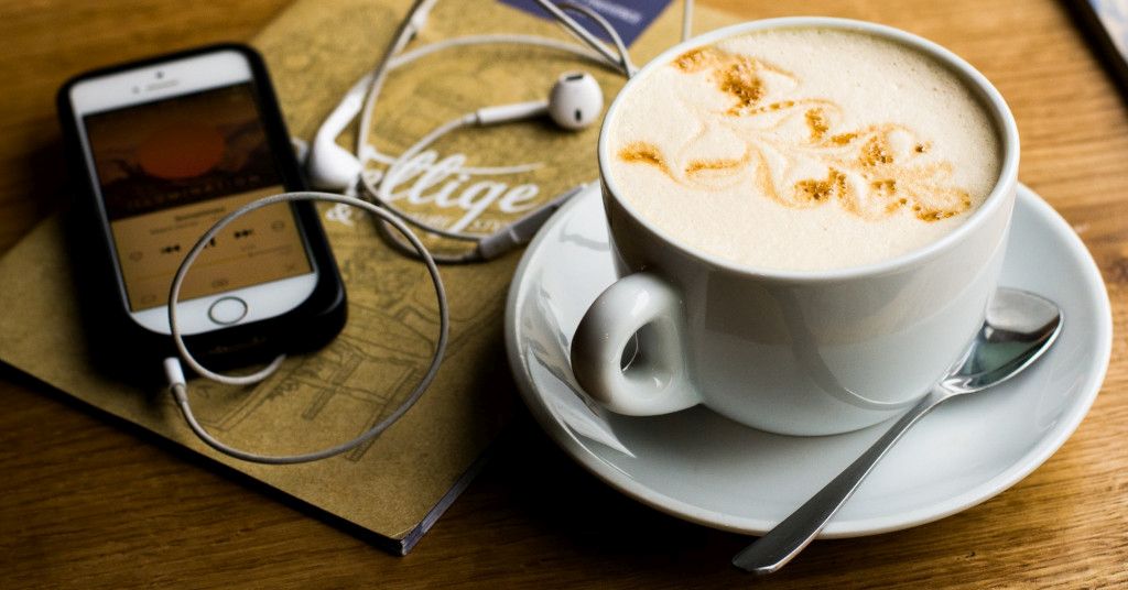 Das Foto zeigt ein Handy mit Kopfhörern neben einer Tasse Kaffee als Sinnbild für die Möglichkeit, sich im Podcast nebenbei auch zu Themen wie Arthrose und Gelenkschmerzen informieren zu können