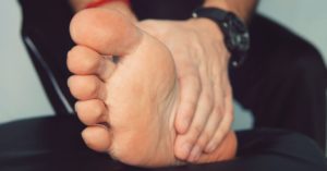 Das Foto zeigt einen Menschen der sich den schmerzenden Fuß hält als Sinnbild für eine Linderung durch die Faszientherapie beim Fersensporn
