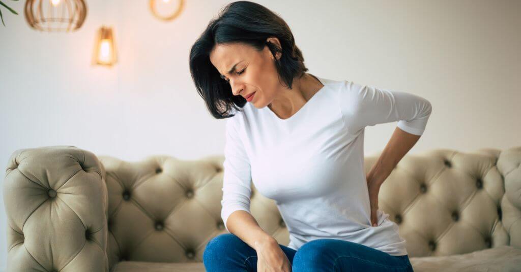 Das Foto zeigt eine Frau die sich den schmerzenden Rücken hält als Sinnbild für eine Linderung durch die Faszientherapie beim ISG-Syndrom