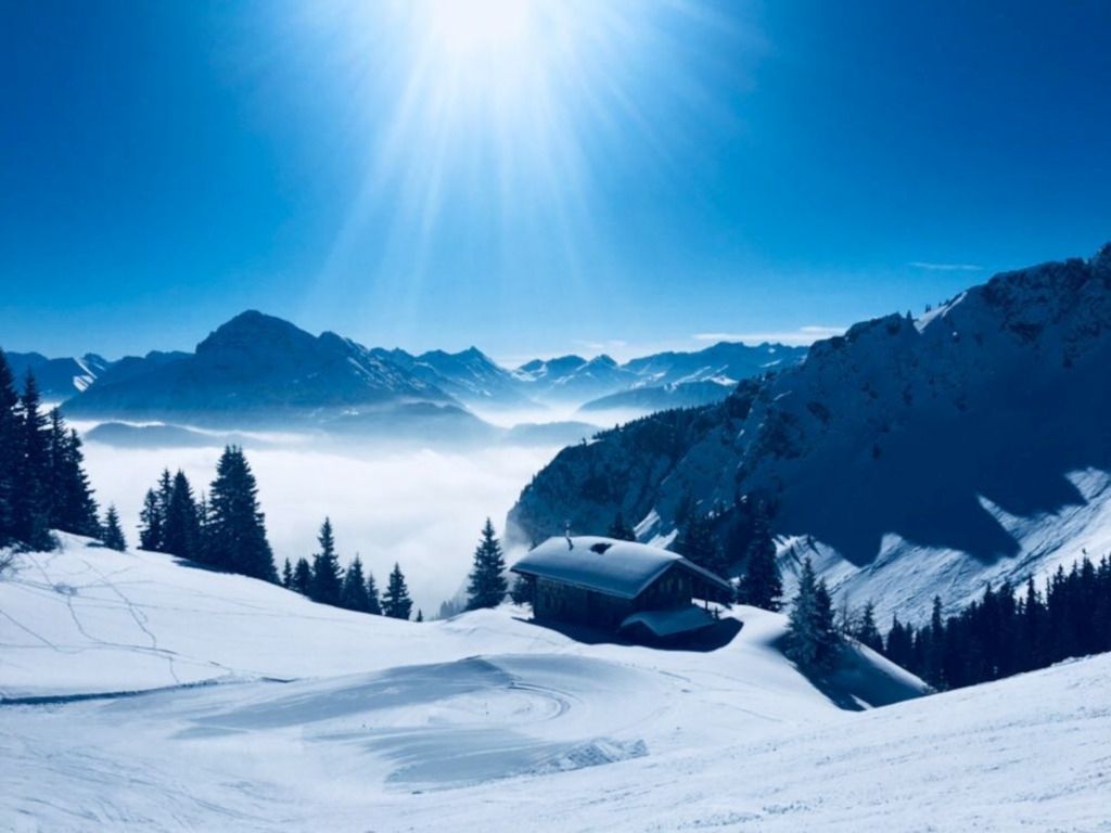 Das Foto zeigt eine Hütte im tiefen Schnee bei tollem Sonnenschein in den Bergen als Sinnbild für den Wintersport ohne körperliche Beschwerden