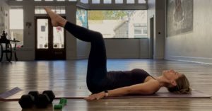 Das Foto zeigt eine Frau bei einer Übung im Liegen als Beispiel für die Anleitung in einem Online Präventionskurs für den gesunden Rücken