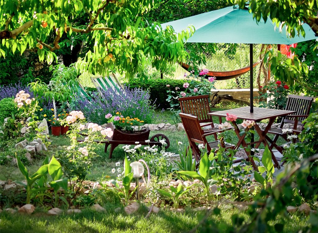 Das Bild zeigt eine Sitzecke mit Sonnenschirm in einem tollen Garten als Sinnbild für die Erholung in einer solchen Wohlfühloase nach der Gartenarbeit als gesunder Bewegung