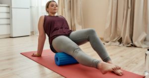 Das Foto zeigt eine junge Frau beim Faszientraining auf einer Matte die vormacht, wie du mit Faszientraining gegen Knieschmerzen vorgehen kannst
