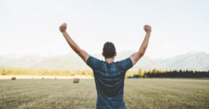 Das Foto zeigt einen stehenden Mann mit erhobenen Armen als Beispiel für eine positive innere Haltung und Wohlbefinden