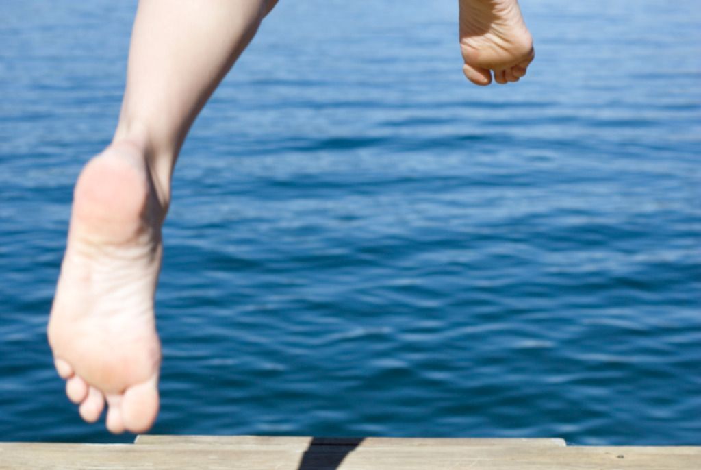 Das Foto zeigt zwei gesunde Füße eines Menschen bei Sprung vom Steg in Wasser als Sinnbild für die erfolgreiche Heilung durch Nahrungsergänzungsmittel nach Knochenbruch