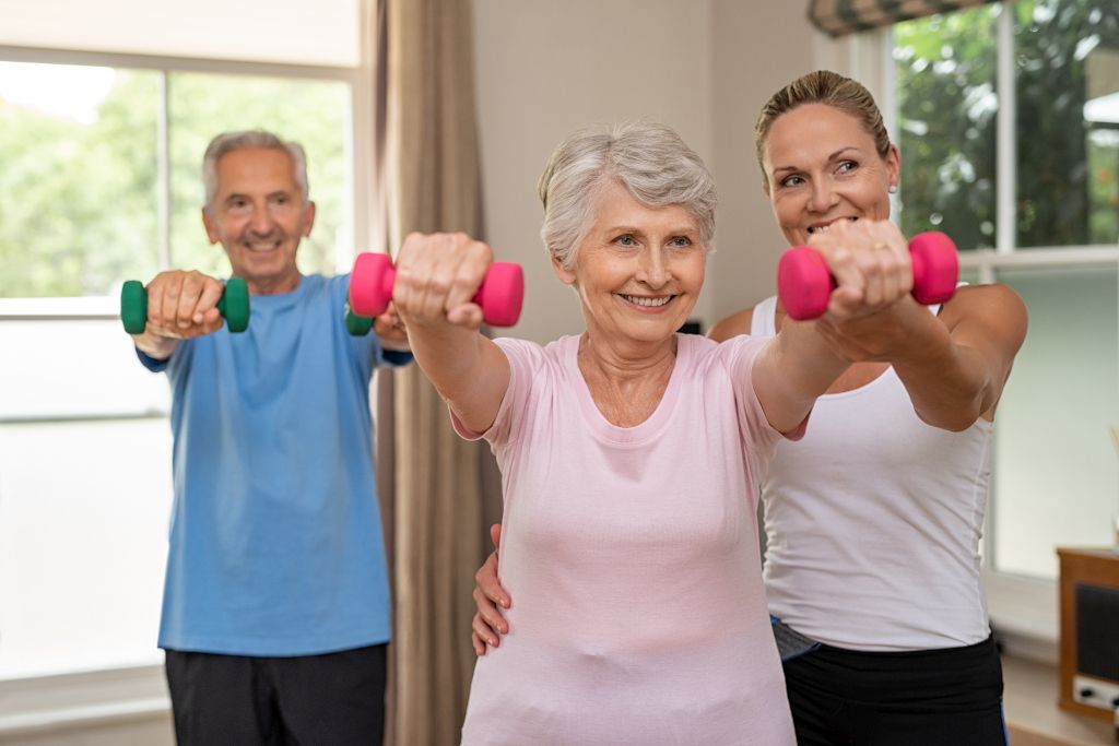 Das Foto zeigt strahlende Senioren bei Übungen mit Anleitung in einem Kurs