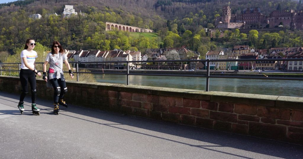 Das Foto zeigt zwei Frauen beim gemütlichen Inlineskating am Neckar mit dem Heidelberger Schloss im Hintergrund