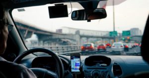 Das Bild zeigt den Blick von hinten auf einen Taxifahrer und sein Navigationssystem al Sinnbild für den Krankentransport, das Rollstuhltaxi oder den Fahrdienst für Senioren