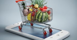 Das Bild zeigt einen Einkaufswagen voll mit Lebensmitteln auf einem Smartphone als Sinnbild für das einfache Bestellen der Lebensmittel im Online Supermarkt
