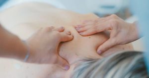 Das Bild zeigt die Hände eines Fachmanns bei der wirksamen und entspannenden Massage für den Rücken im Schulter- bzw. Nackenbereich.