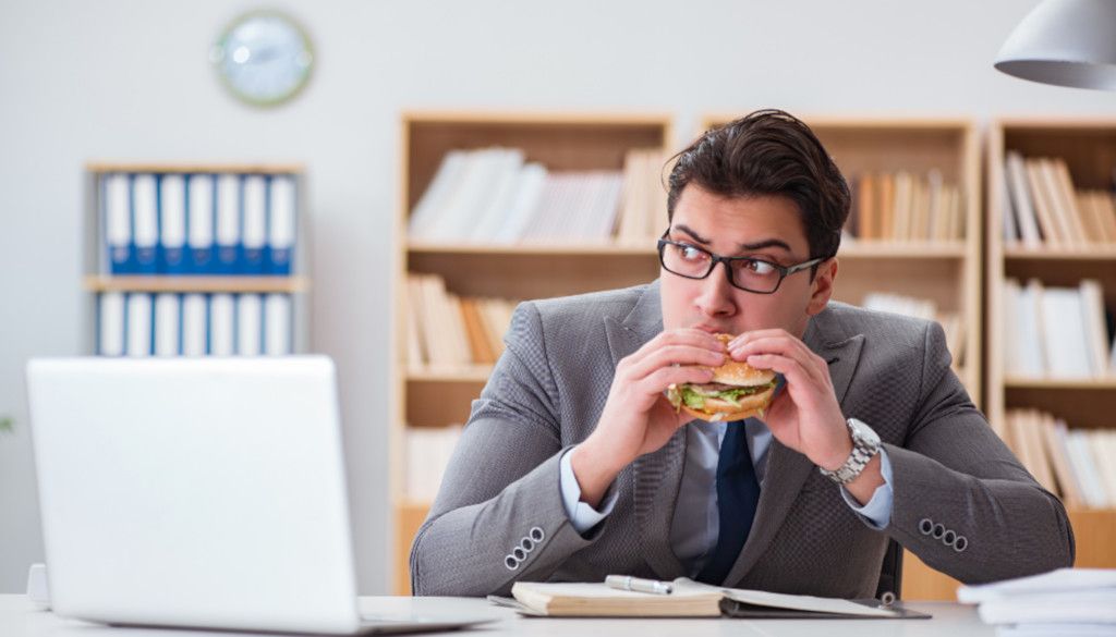 Das Foto zeigt einen Mann beim Snack im Büro als Sinnbild wie die Progressive Muskelentspannung gegen emotionales Essen helfen kann.