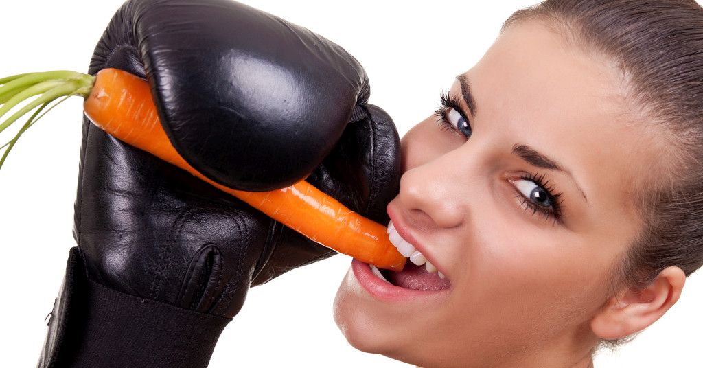 Das Bild zeigt eine Frau mit Boxhandschuh eine Möhre essen als Sinnbild für die Bedeutung der richtigen Ernährung für das Immunsystem