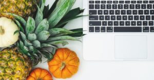 Das Foto zeigt unterschiedliche Obst- und Gemüsearten neben einem Laptop als Sinnbild für das Thema Nachhaltigkeit bei Lebensmitteln