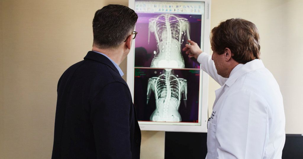 Das Foto zeigt einen Mann bei der gemeinsamen Betrachtung einer Röntgen-Aufnahme einer Wirbelsäule mit seinem Arzt als Sinnbild für die Vorteile den Sportcheck der Sportmedizin zu nutzen