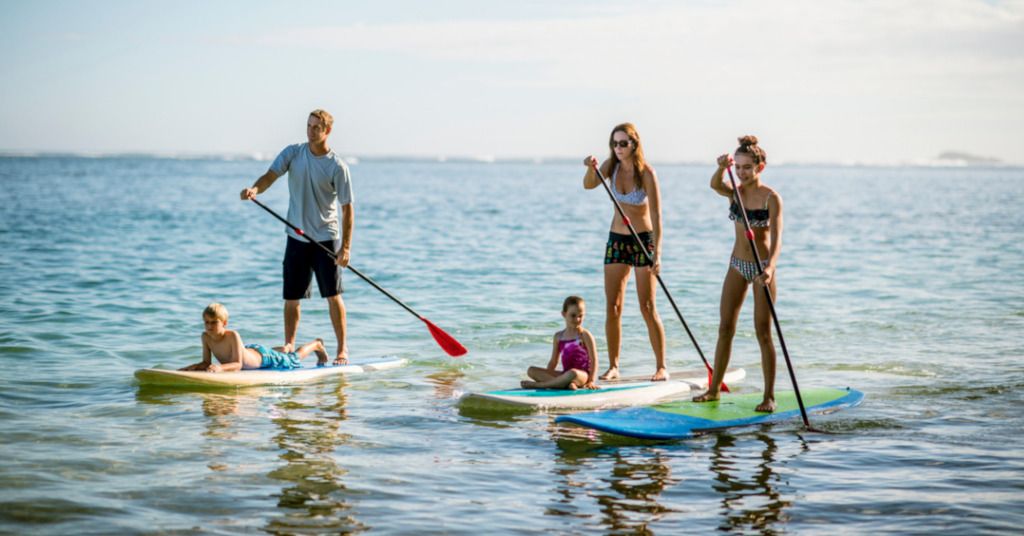 Das Foto zeigt eine Familie beim gemeinsamen Stand Up Paddling im ruhigen und warmen Meer