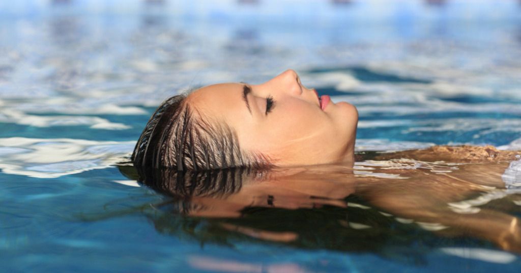 Das Bild zeigt eine tiefenentspannte Frau im Wasser liegen als Sinnbild für die erreichbare Entspannung durch therapeutische Anwendungen mit, im und durch Wasser