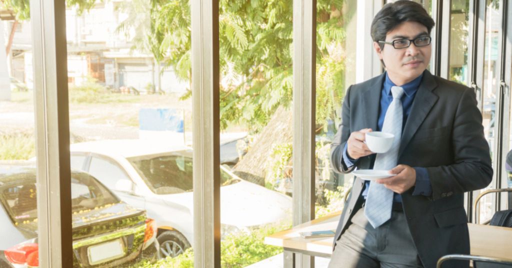Das Bild zeigt einen Geschäftsmann mit Kaffeetasse an einem Besprechungstisch lehnen als Sinnbild für die vielen kleinen Gelegenheiten, im beruflichen Alltag etwas Bewegung in die Abläufe am Arbeitsplatz zu bekommen