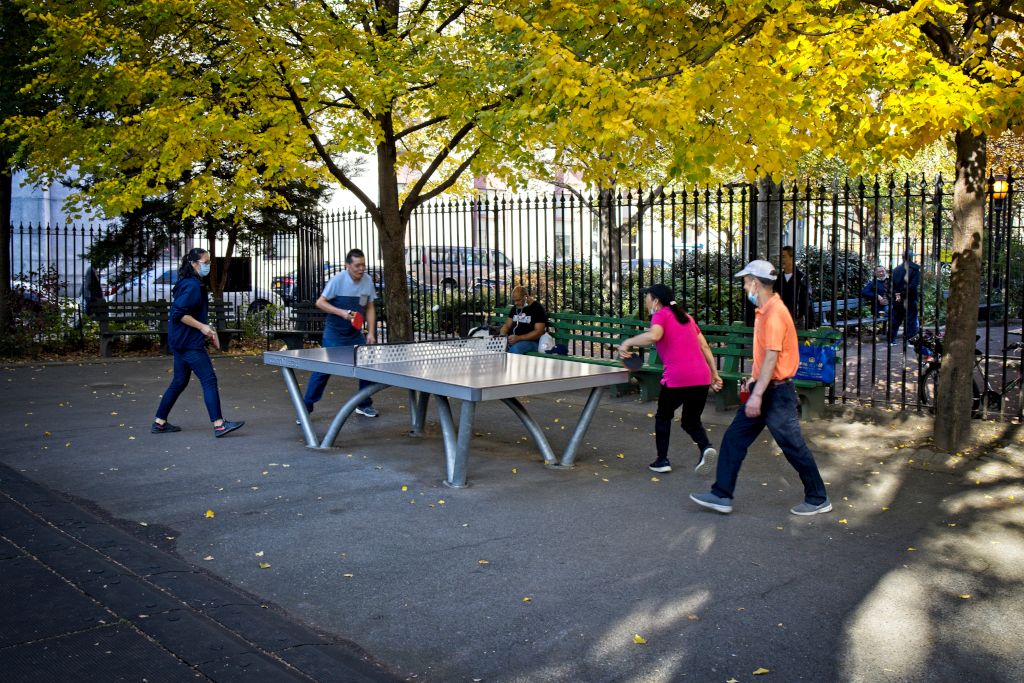 Das Foto zeigt vier Menschen, die auf einer öffentlichen Platte in einem schönen Park Tischtennis spielen