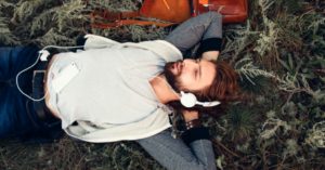 Das Bild zeigt einen Mann mit Kopfhörern auf dem Waldboden liegen als Sinnbild für die einfache Möglichkeit, mit guten Übungen auf CD zwischendurch zu entspannen
