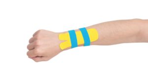 Das Bild zeigt einen Arm mit aufgeklebten Tape-Streifen am Handgelenk als Sinnbild für die Linderung durch Kinesio-Tapes bei Beschwerden an Hand und Arm