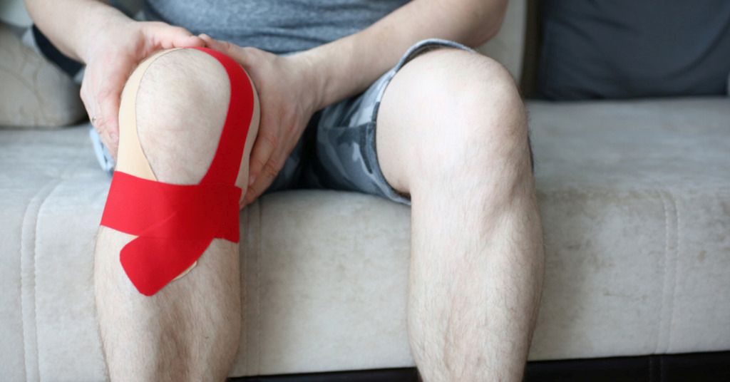 Das Bild zeigt ein Knie mit aufgeklebten Tape-Streifen als Sinnbild für die Linderung durch Kinesio-Tapes bei Beschwerden am Knie
