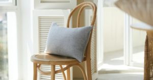 Das Bild zeigt ein festes Kissen auf einem einfachen Holzstuhl als Sinnbild für Kissen zur Unterstützung der Wirbelsäule beim Sitzen