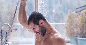 Das Bild zeigt einen Mann mit Handbrause beim Duschen als Sinnbild für die Entspannung durch ein Luftsprudelbad, eine Massagebrause oder einen Luffaschwamm