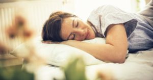 Das Bild zeigt eine entspannt schlafende Frau auf einem Kissen als Sinnbild für den erholsamen und gesunden Schlaf mit dem richtigen Nackenkissen oder Seitenschläferkissen