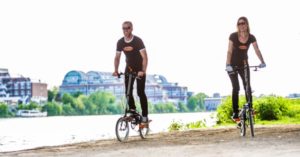 Das Bild zeigt einen Mann und eine Frau auf Zweiradsteppern am Fluss als Sinnbild für den Spaß am Outdoor Sport und Training wenn die richtigen Fitnessgeräte eingesetzt werden