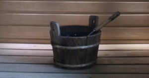 Das Bild zeigt einen hölzernen Wassereimer mit Schöpfkelle als Sinnbild für die Sauna zuhause