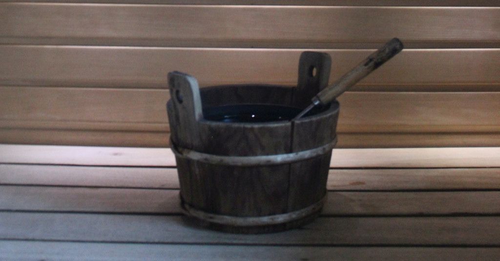 Das Bild zeigt einen hölzernen Wassereimer mit Schöpfkelle als Sinnbild für die Sauna zuhause