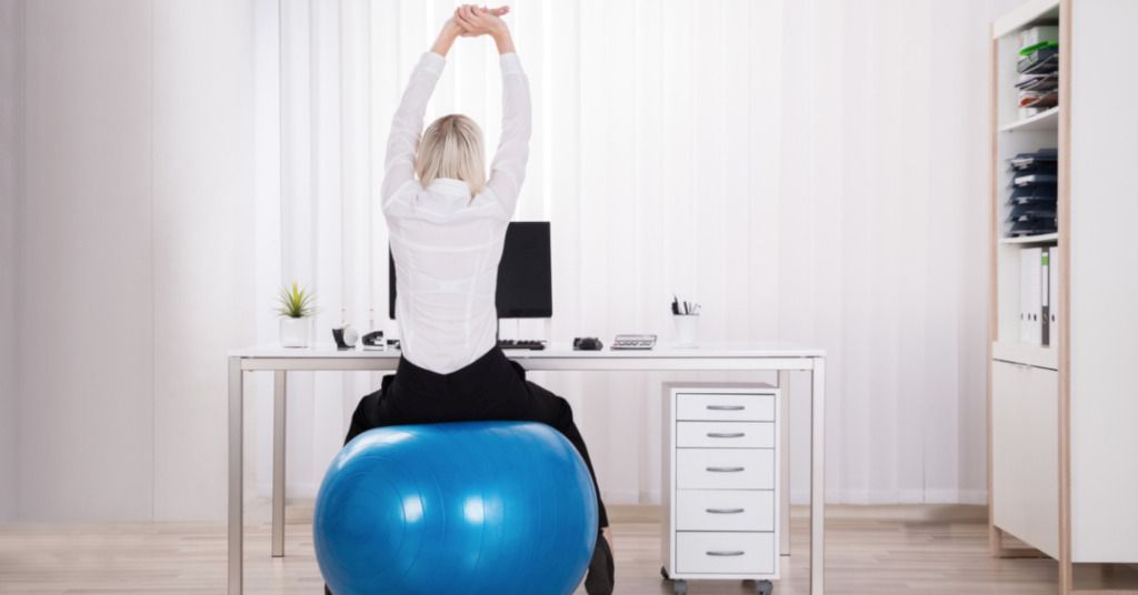 Das Bild zeigt eine Frau auf einem Sitzball am Schreibtisch als Sinnbild für die gesunde Bewegung nebenbei durch Sitzbälle, Ballkissen oder Fitnesshocker