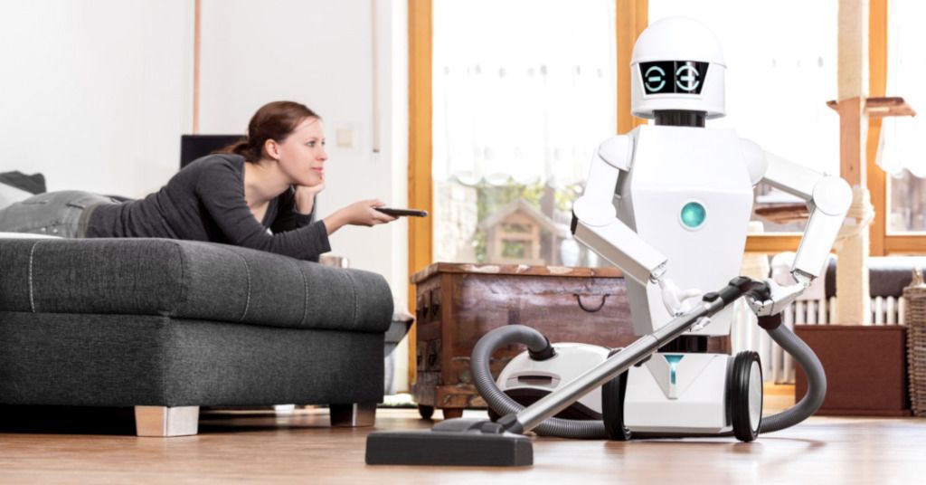 Das Bild zeigt eine Frau bei der Pause auf dem Sofa während ein Roboter die Hausarbeit erledigt: So kannst du Smart-Home Systeme von Alexa bis zum Mähroboter zu deiner Entlastung nutzen