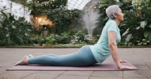 Das Bild zeigt eine Frau bei Dehnübungen auf einer Matte im Garten als Sinnbild für die Themen Stretching und Triggerpunktmassage