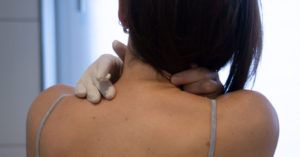 Das Foto zeigt einen Menschen der sich mit einem Gummihandschuh eine Salbe auf den Nacken aufträgt als Sinnbild für die Linderung durch eine Wärmebehandlung mit einer guten Wärmesalbe oder Wärmecreme