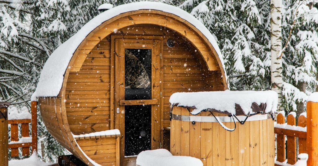 Das Bild zeigt eine Fassauna im verschneiten Garten als Sinnbild für die tollen Möglichkeiten eine Fasssauna oder mobile Sauna im eigenen Zuhause zu nutzen