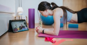 Das Bild zeigt eine junge Frau beim Online Training auf einer Yogamatte vor dem Laptop zuhause
