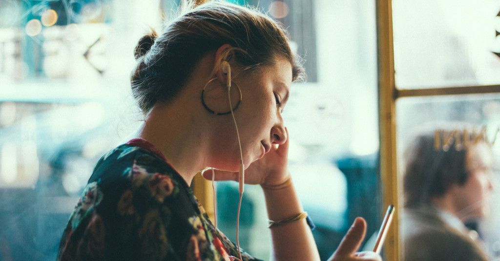 Das Bild zeigt eine Frau mit Kopfhörern im Cafe als Sinnbild für die Vorzüge sich mit dem Podcast 