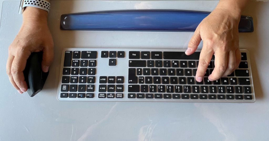 Das Bild zeigt eine zwei Hände bei der Arbeit am Computer mit ergonomischer Maus, Tastatur und Handgelenkauflage als Sinnbild für die Entlastung der Hände und Arme durch ergonomische Arbeitsmittel im Büro