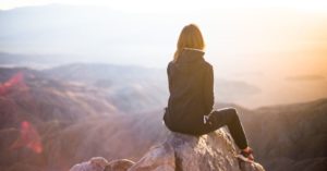 Das Bild zeigt einen Menschen auf einer Bergspitze bei tollem Sonnenschein mit weitem Blick über die Täler bis zum Meer als Sinnbild für die Chancen, Resilienz gegen ungesunden Stress aufzubauen