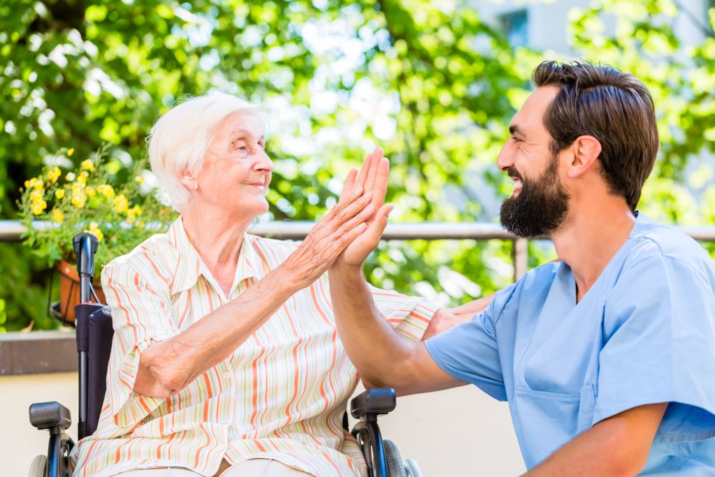 Das Bild zeigt einen Pfleger und eine Seniorin beim lachenden Abklatschen als Sinnbild für die Bedeutung der Gesundheitsförderung für Mitarbeitende in der Pflege
