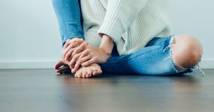 Das Bild zeigt einen sitzenden Menschen der sich den schmerzenden Fuß hält als Sinnbild für die Möglichkeiten der Faszientherapie zur Linderung bei Fußschmerzen