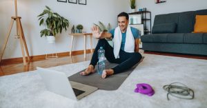 Das Bild zeigte einen Mann nach dem Fitnesstraining vor dem Laptop im Wohnzimmer als Sinnbild für die Möglichkeiten zum Online Gesundheitssport zuhause im zertifizierten Gesundheitskurs