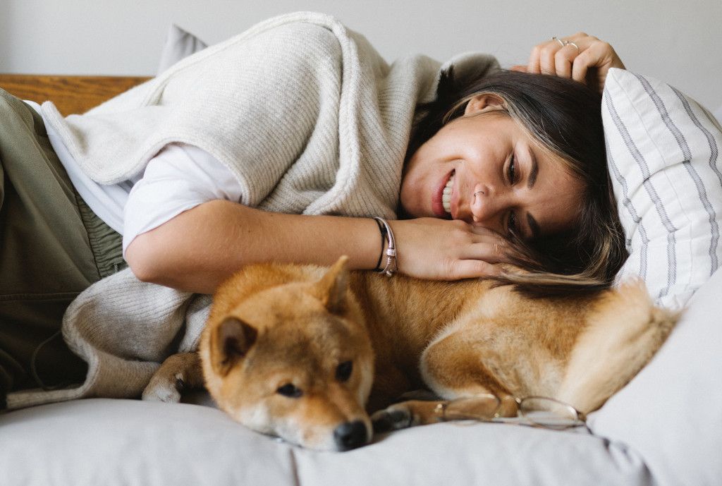 Das Bild zeigt eine Frau beim Kuscheln mit dem Hund auf einem Sofa als Sinnbild für den Beitrag der Sinnlichkeit zur Stressbewältigung