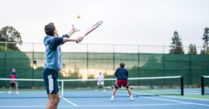 Das Bild zeigt 4 Menschen beim Tennis-Doppel auf einem Außenplatz als Sinnbild für Tennis als tollem Gesundheitssport