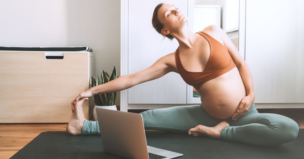 Das Bild zeigt eine Schwangere beim Pilates zuhause vor dem Laptop als Sinnbild für die Vorteile von Pilates als Sport und Bewegung in der Schwangerschaft