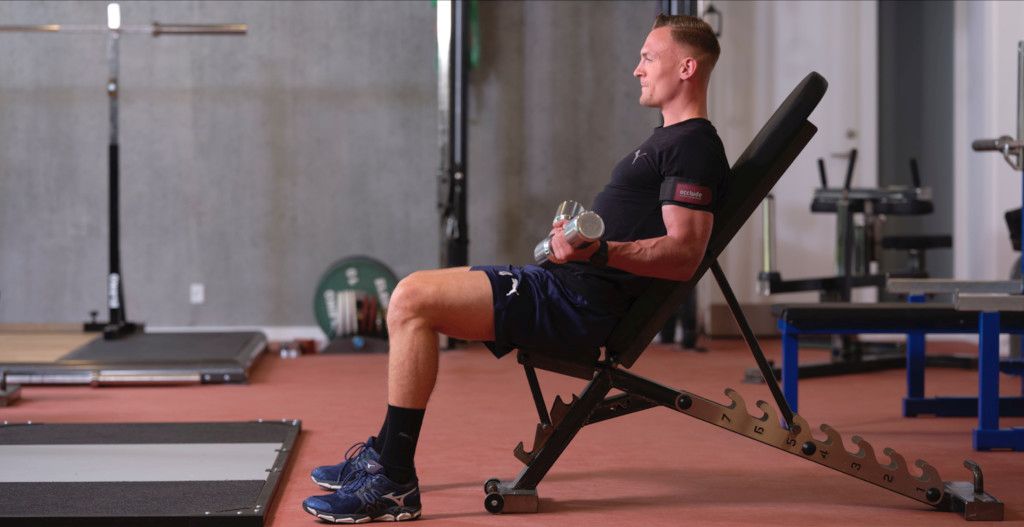 Das Bild zeigt einen Sportler mit Oberarmmanschette beim Krafttraining der Arme als Sinnbild für das Blood-Flow Restriction (BFR) Training