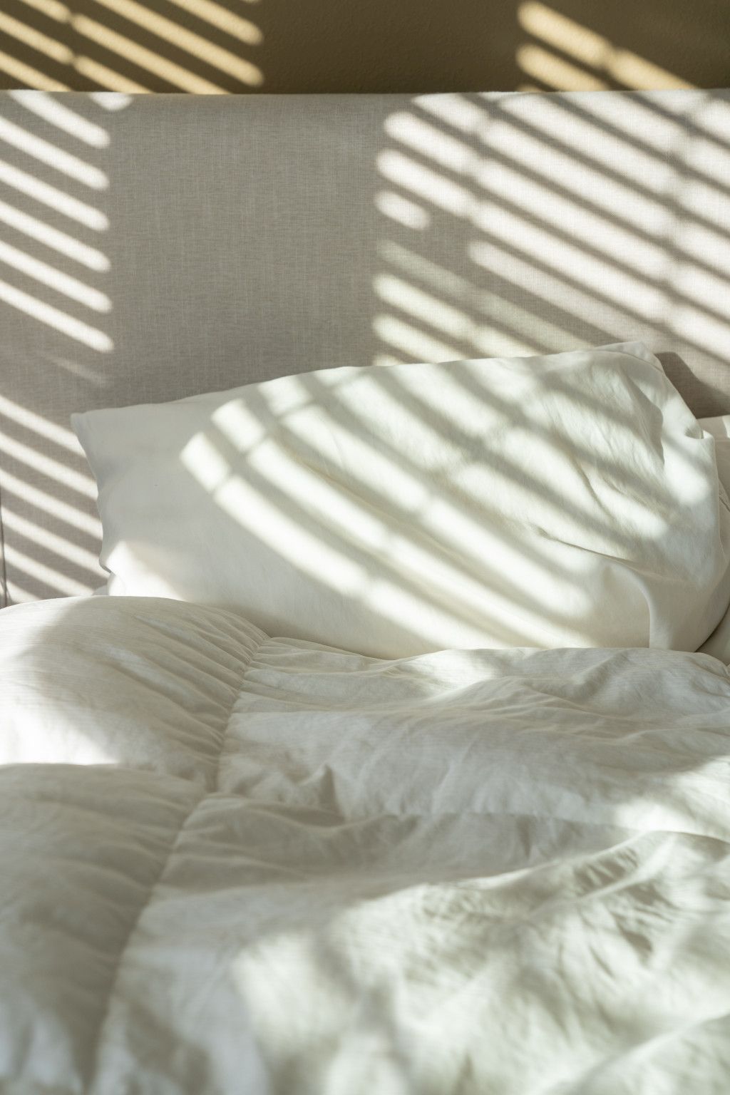 Das Bild zeigt ein Bett im Sonnenlicht als Sinnbild für ein unbeschwertes Erwachen nach gutem Schlaf ohne Verspannungen im Nacken oder Rücken