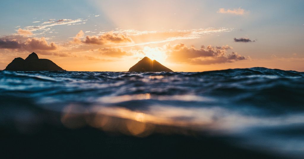 Das Bild zeigt Felsen im Meer vor einem Strand im Sonnenuntergang als Sinnbild für die hawaiianische Huna Lehre