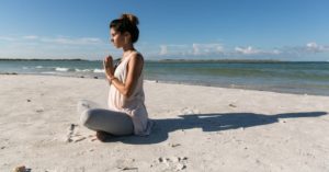 Das Bild zeigt eine schwangere Frau beim entspannten Yoga am sonnigen Strand als Sinnbild für die Ruhe und Kraft in der Schwangerschaft durch Schwangerschaftsyoga im Online Kurs